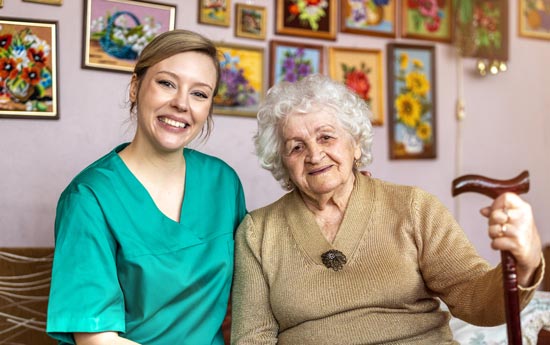 female nurse and senior patient smiling on couch in home