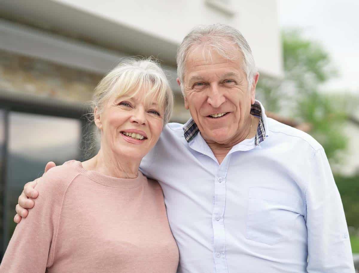 retired couple smiling while embracing with their home in the background