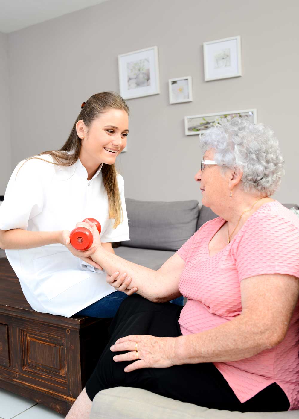 senior woman performing a bicep curl at home with assistance of a rehabilitation provider